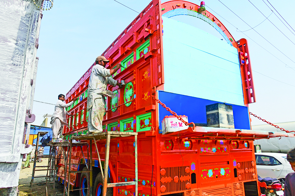 Artist Haider Ali (left) works on a truck at a workshop in Karachi.<br>