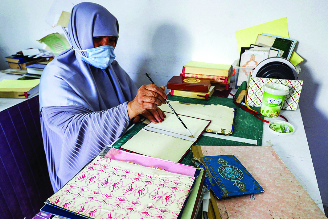 A woman places glue with a brush on the hardcover binding for a volume of the Holy Quran.