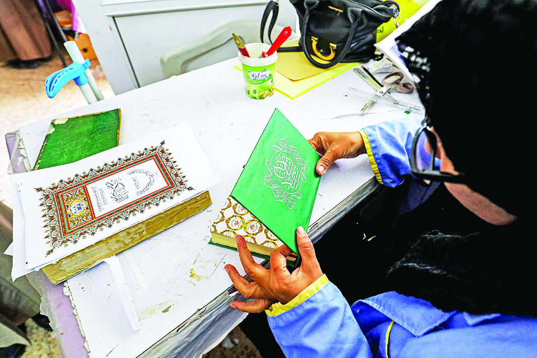 A woman binds with glue a hardcover for a volume of the Holy Quran.