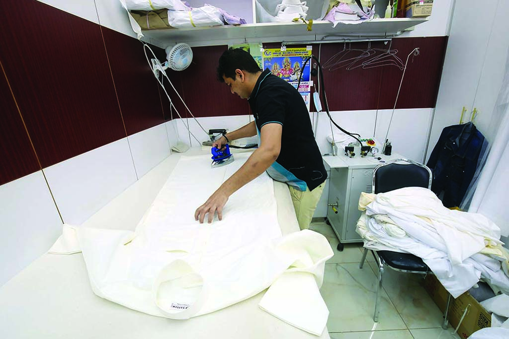 A tailor irons a dishdasha inside his shop.