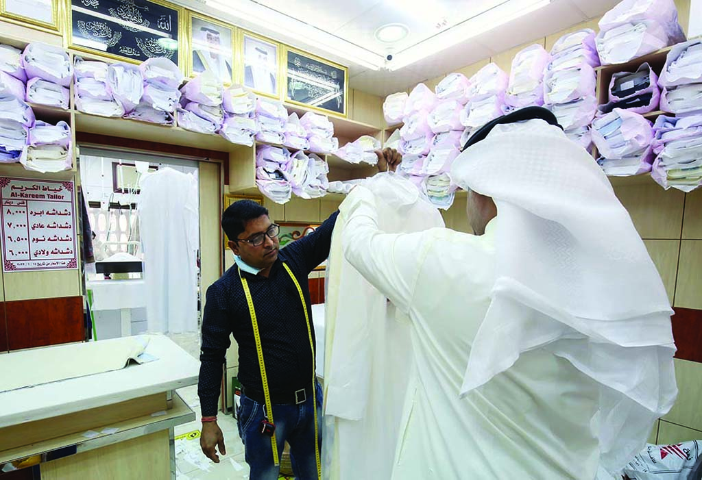 A tailor hands a dishdasha to a customer.