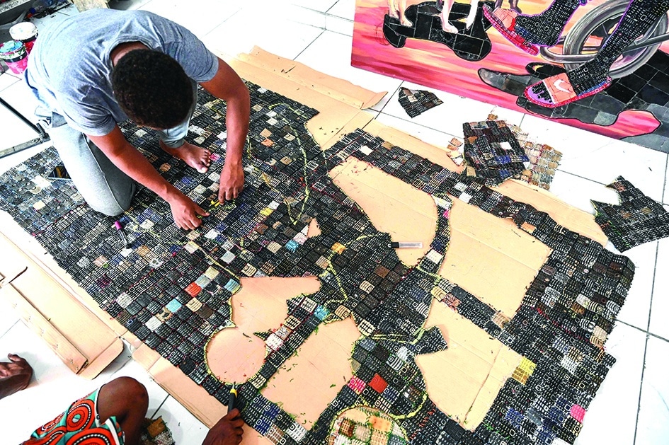 Ivorian artist Mounou Desire Koffi cuts out an image on the screen of his artwork reproduced on a carpet of used telephone keyboards in Bingerville.