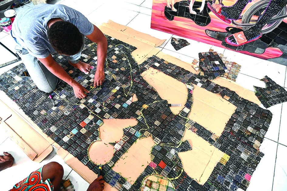 Ivorian artist Mounou Desire Koffi cuts out an image on the screen of his artwork reproduced on a carpet of used telephone keyboards in Bingerville.