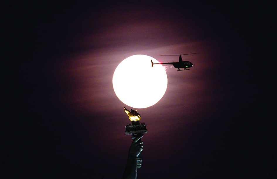 In this file photo a helicopter flies past as the full moon rises behind the Statue of Liberty in New York City.