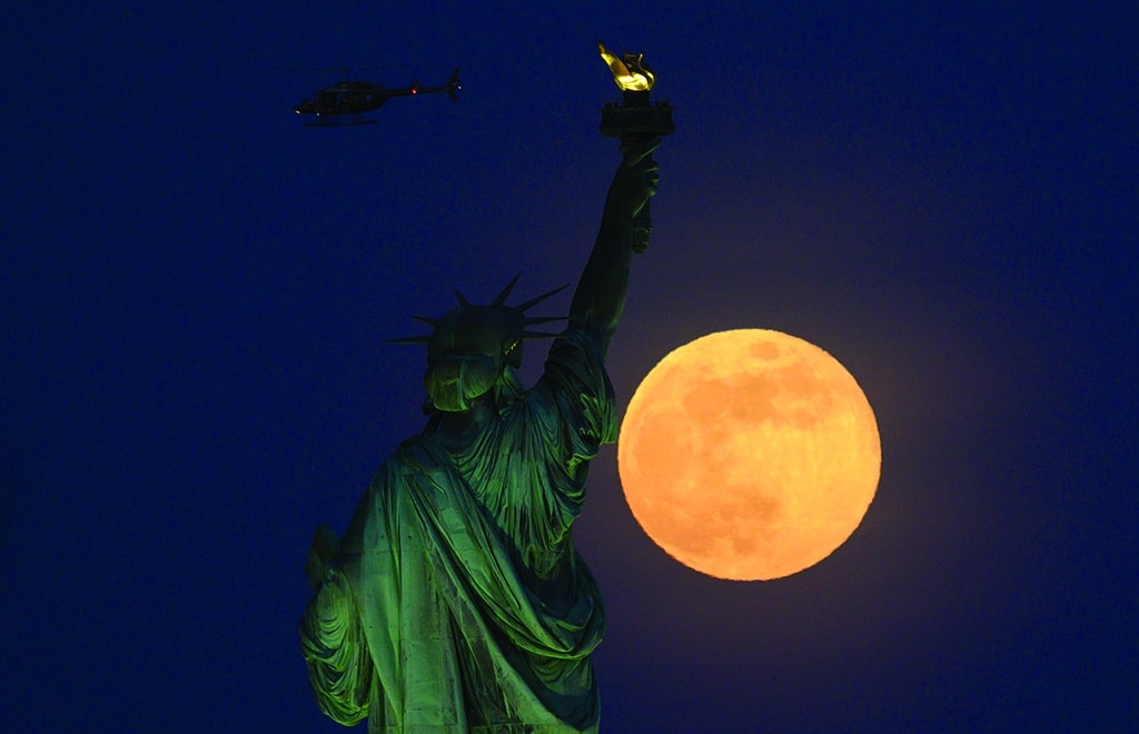 In this file photo a helicopter flies past as the full moon rises behind the Statue of Liberty in New York City.