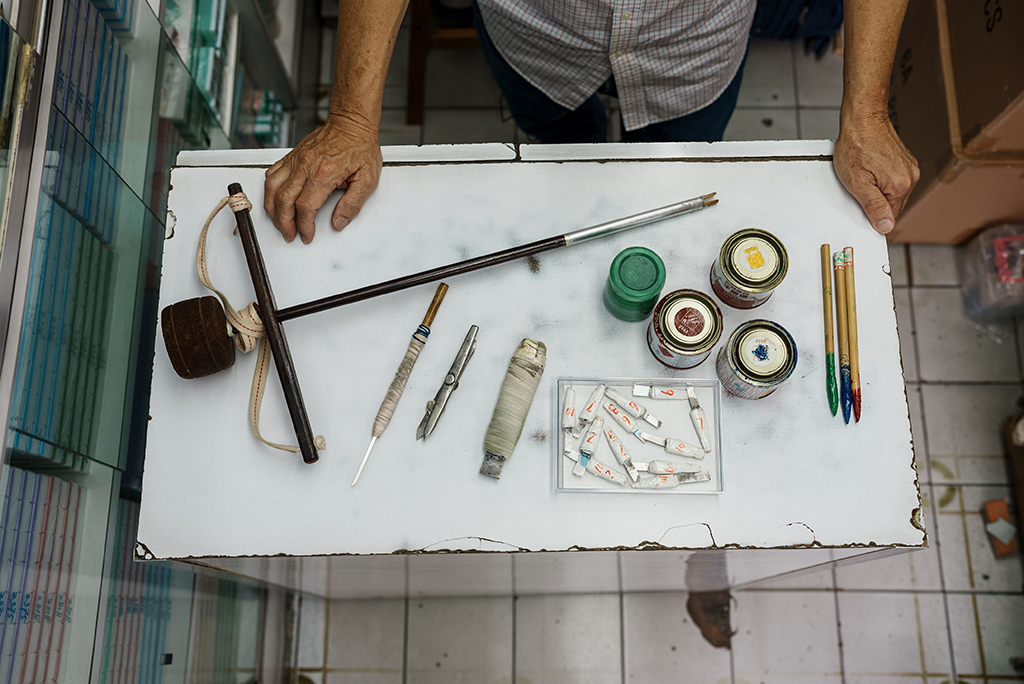 Mahjong tile artisan Cheung Shun-king displaying his tool set, including a drill stand, carving knives, writing brushes and paint, used to make hand-carved mahjong pieces, at his shop in the Yau Tsim Mong district of Hong Kong.