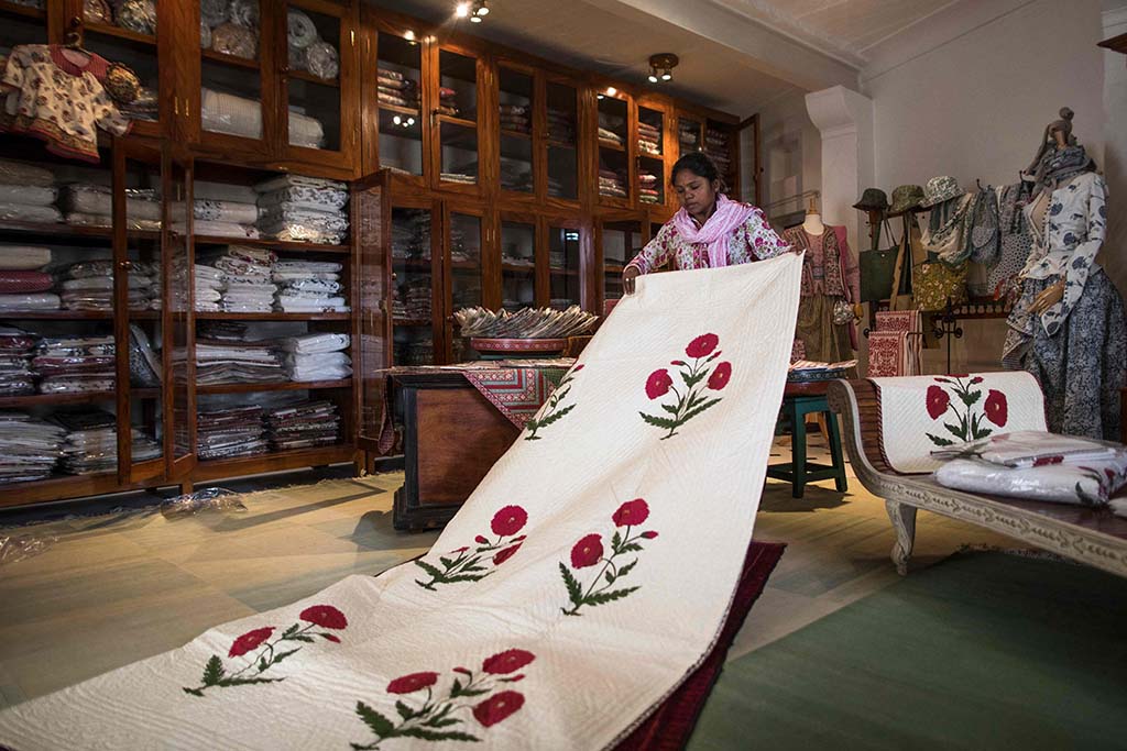A worker displays a quilt with a hand block printing design of a poppy flower, rendited from an original design of the 17th century made for Mughal emperor Shah Jahan.