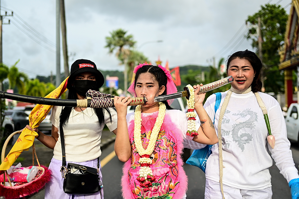 A devotee (center) of the Jor Soo Gong Naka shrine with a sword pierced through her cheek takes part in a procession during the annual Vegetarian Festival in Phuket. 