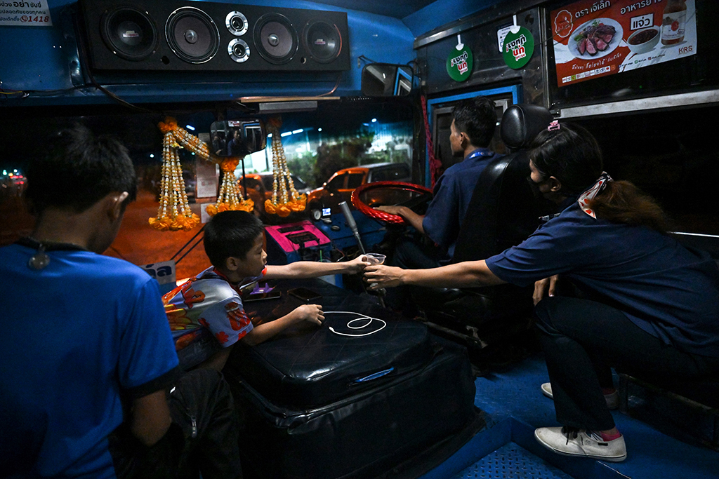 Bus conductor Arunee On-sawats being handed a coffee from her son as her husband Aphisak Sodmui drives the No.8 bus out of the garage before dawn in Bangkok.