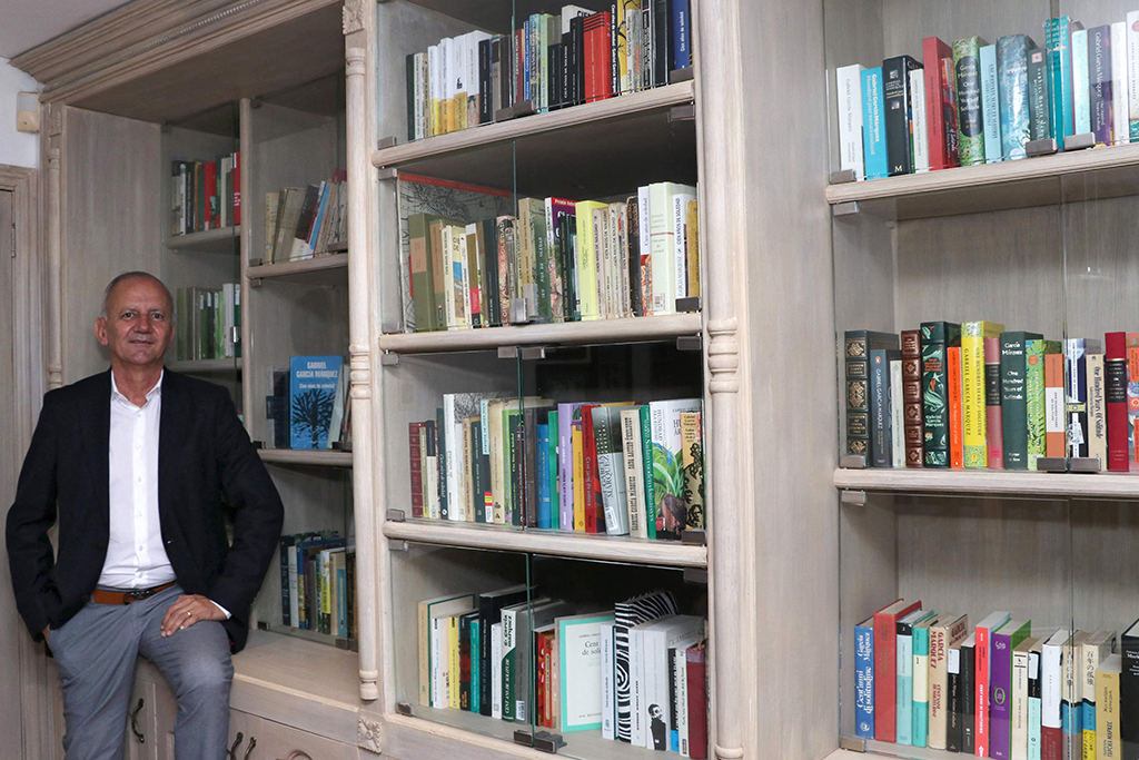 Jorge Salazar poses next to his bookshelf full of international editions of