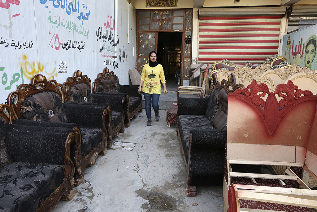 Iraqi carpenter Nour Al-Janabi walks next to pieces waiting to be renovated at her home furniture workshop in Baghdad's Abu Dsheer area.