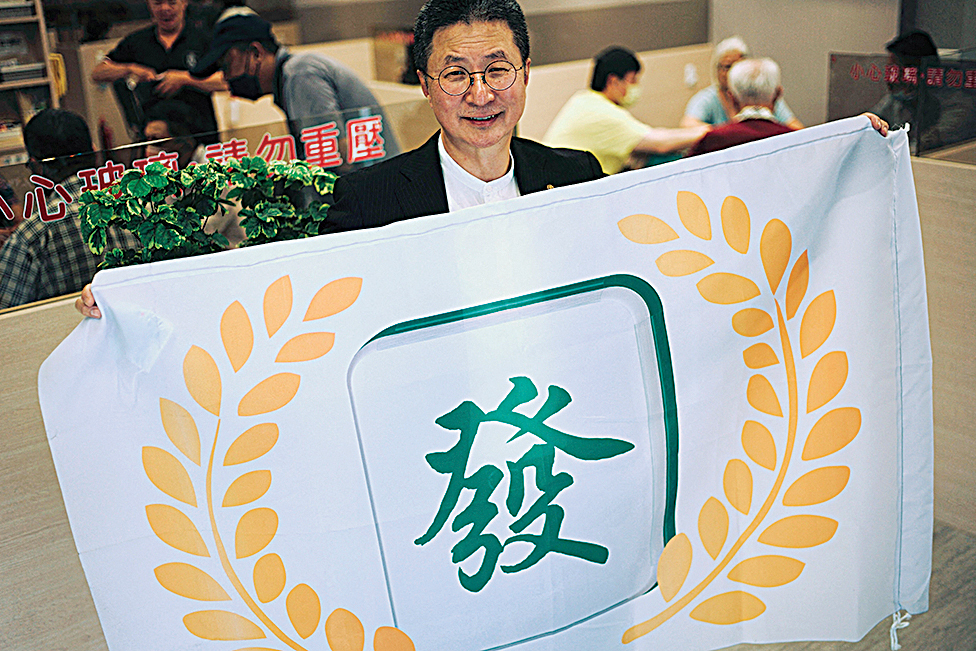This picture shows Kuo Hsi (center), founder of Taiwan’s Mahjong the Greatest party, posing with his party flag at his parlor in Kaohsiung. 