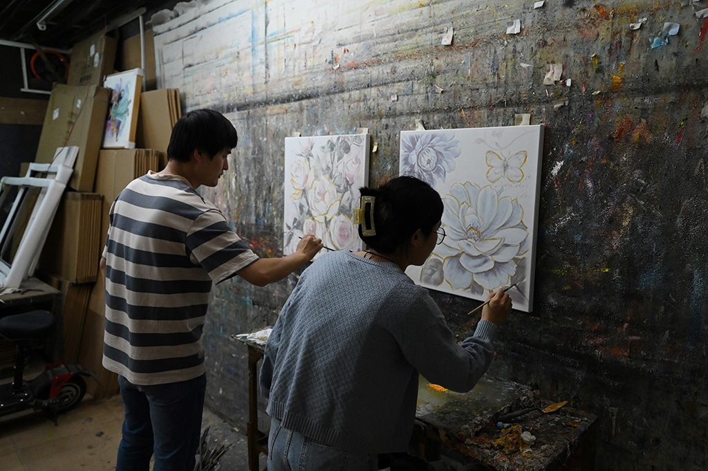 Artists paint on top of pre-printed art works in a workshop at Dafen village.