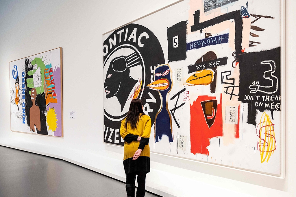 A visitor stands next to “Mind Energy” (Left), as she looks at “Pontiac No. 5”, two paintings made in 1985 by artist Jean-Michel Basquiat and US artist, Andy Warhol (1928-1987), during a preview of the exhibition “Basquiat X Warhol”.