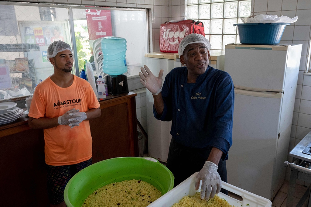 Brazilian chef Carlos Alberto da Silva (R), known as Nego Breu, speaks while cooking food to be delivered to the homeless population of the city center of Rio de Janeiro at the restaurant Chapeu do Chef, at the Chapeu Mangueira favela.