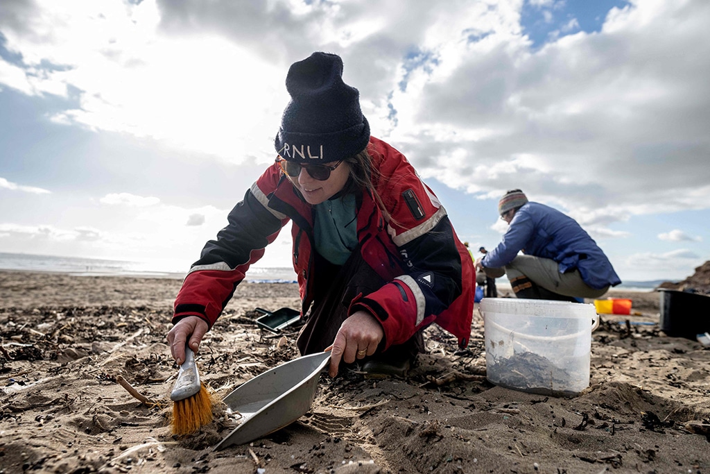 A volunteer uses a brush as she takes part in a beach clean organised to collect nurdles and other plastic waste on the Tregantle beach.