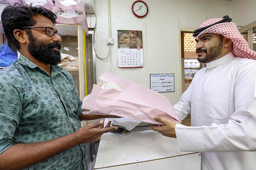 A tailor hands over a customer his order of dishdashas after a waiting period of a month and a half.