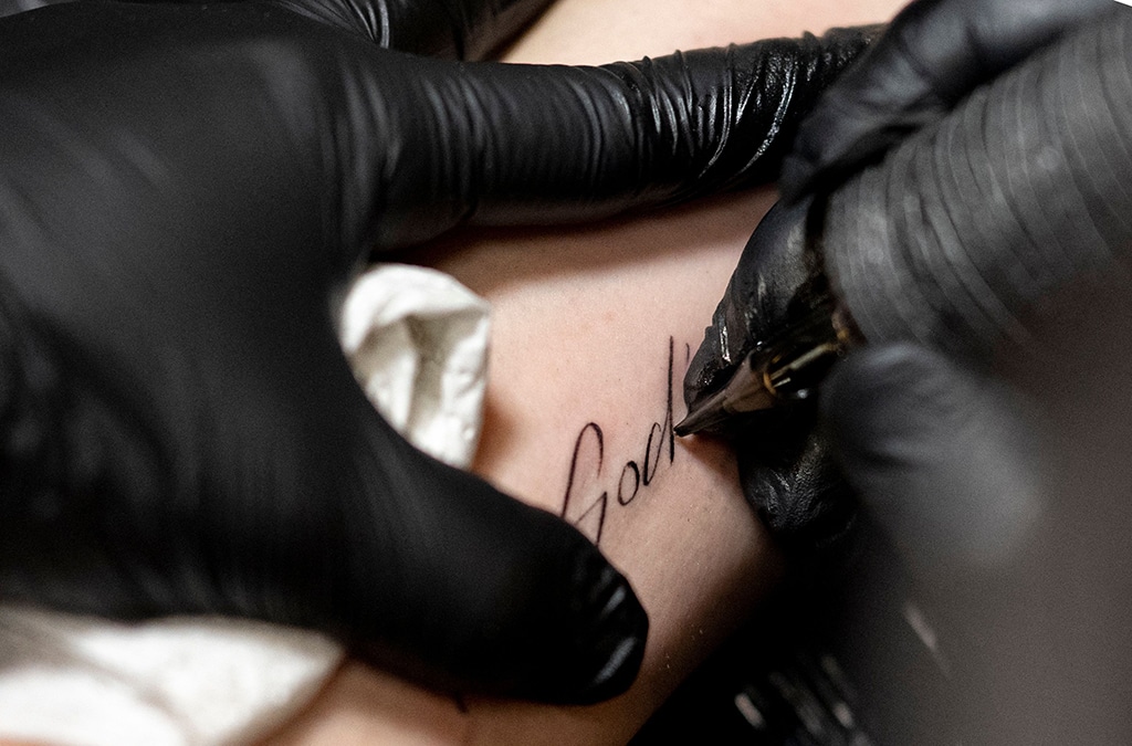 Tattoer Silas Becks puts protective patch over a tattoo reading 'In God's hands..' on the arm of a young man in Vienna, Austria.