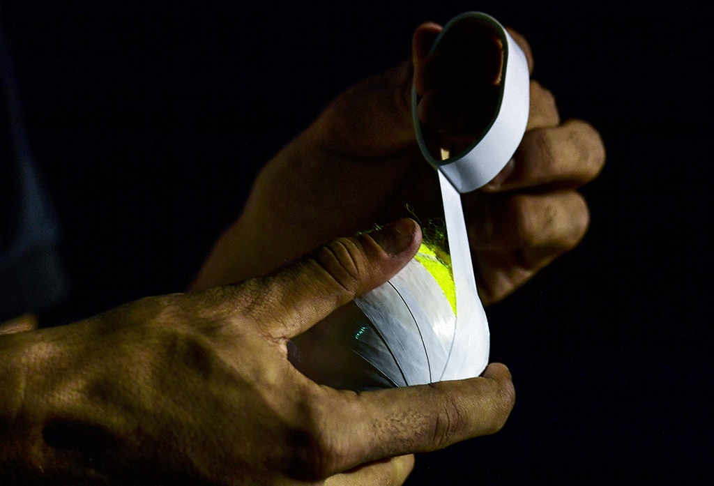 A young cricketer wraps electric tape on the tennis ball before the start of the tape ball night cricket tournament.