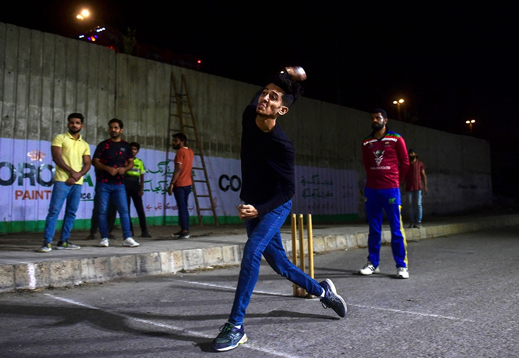 A cricketer delivers a ball during the tape ball night cricket tournament.