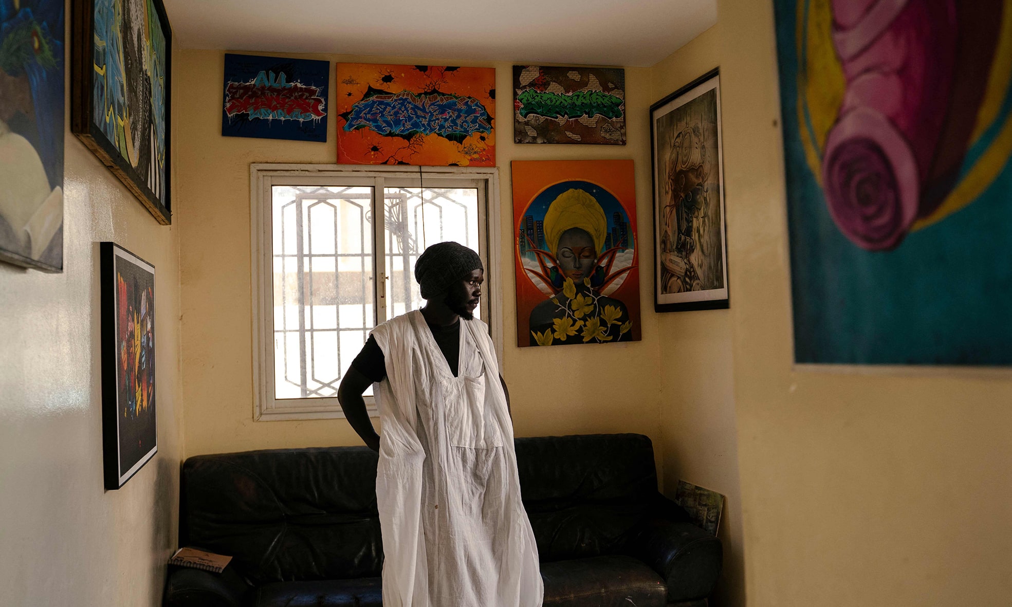 Cherif Tahir Diop poses surrounded by paintings in the hallway of RBS Akademya.