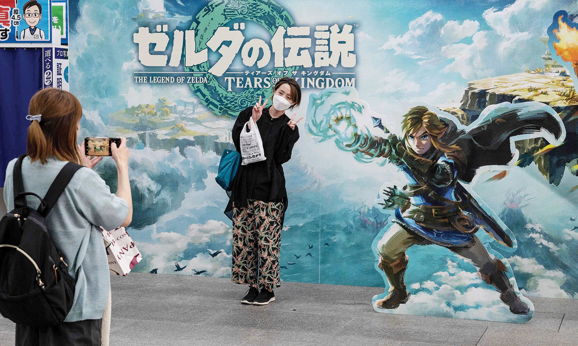 A woman poses for a photo at a display outside a popular electronics chain store advertising the latest offering from Japanese gaming giant Nintendo's long-running 'Legend of Zelda' game series - 'Tears of the Kingdom' .