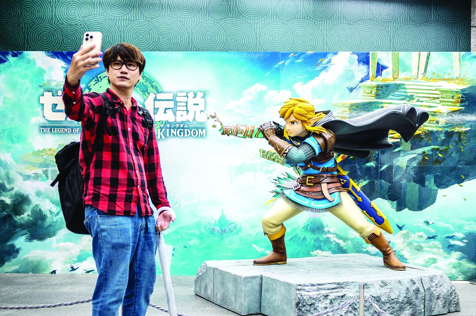 A visitor posing next to a statue of a character from Japanese gaming giant Nintendo's video game 'The Legend of Zelda: Tears of the Kingdom' on display.
