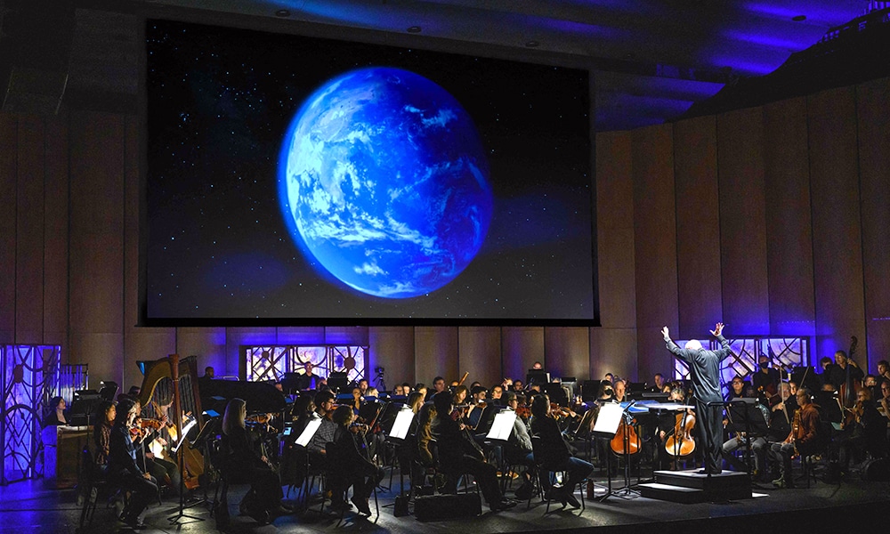 In front of an NASA image projected on a screen, National Philharmonic Music Director and Conductor Piotr Gajewski rehearses 'Cosmic Cycles, A Space Symphony' by composer Henry Dehlinger.