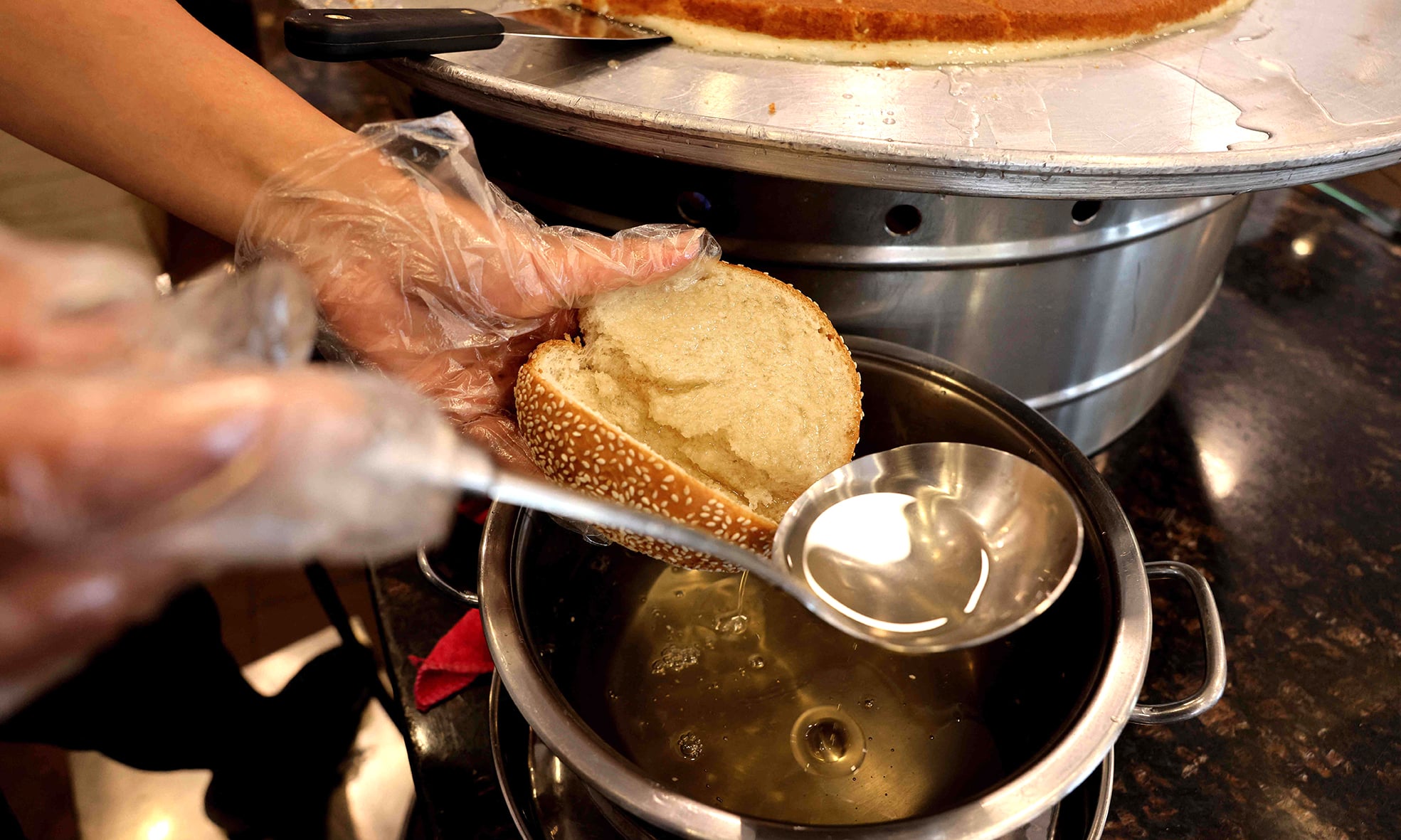 A worker pours syrup on a bun as she sells traditional dessert Kunafa, at a shop in Byblos.