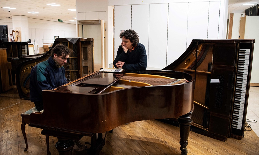 Artist and Musician Tim Vincent-Smith (right), Co director of Painodrome, a charity centre aiming a the refurbishing and repairing pianos, listens to a volunteer trying a piano in their atelier.