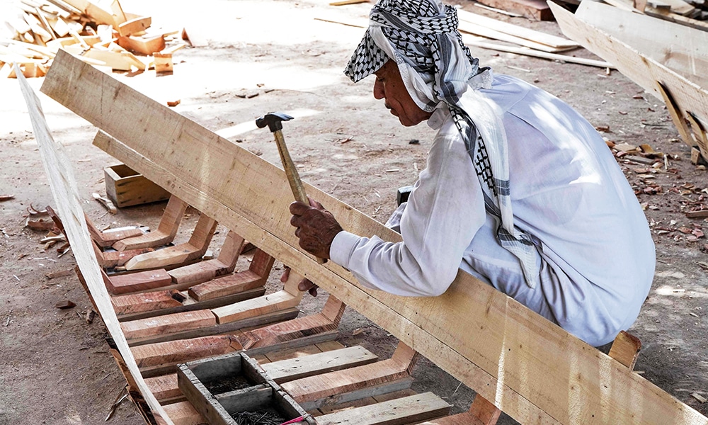 A carpenter hammers beams as he builds a traditional 'meshhouf' wooden boat at a workshop.