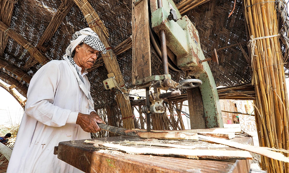 A carpenter uses an electric saw to cut wood as he builds a traditional 'meshhouf' wooden boat at a workshop.