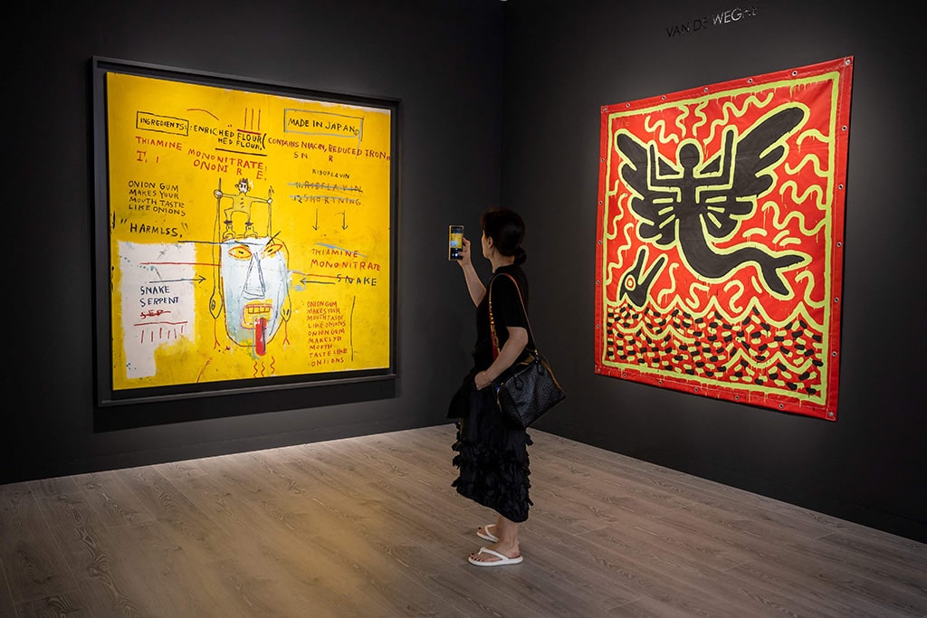 A woman takes a picture of 'Onion gum' 1983 by US artist Jean-Michel Basquiat (left) next to 'Untitled' 1982 by US artist Keith Haring at the Van de Weghe fine art gallery during Art Basel.