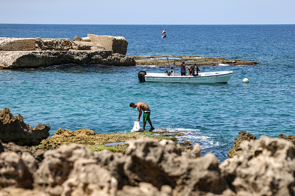 Scuba divers sit in a boat in the Mediterranean sea by rocky structures off Lebanon's northern coastal village of Kfarabida.